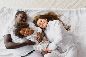 excité multiracial Jeune famille avec peu fille enfant avoir amusant, fou de joie heureux. international maman et papa jouer avec petit fille, prendre plaisir fin de semaine à Accueil ensemble photo