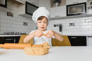 peu garçon portion le sien mère avec le cuisson dans le cuisine permanent à le compteur aux côtés de sa pétrissage le pâte pour le tarte photo