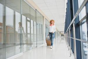 fille voyageur en marchant avec porter tenir valise dans le aéroport. touristique concept. femme des promenades par aéroport Terminal avec bagage. Voyage concept photo