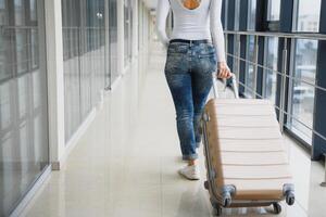 fille voyageur en marchant avec porter tenir valise dans le aéroport. touristique concept. femme des promenades par aéroport Terminal avec bagage. Voyage concept photo