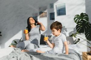 maman avec fils dans pyjamas en buvant jus dans le Matin dans lit. en bonne santé en mangeant concept photo