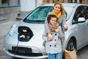 élégant mère et fille charge un électrique voiture, et dépenser temps ensemble. photo