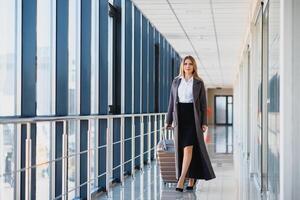 élégant femme d'affaires avec bagage à le aéroport.. attrayant Dame avec Voyage valise en marchant le long de aéroport attendre pièce Stock photo