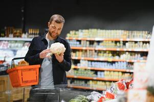 client dans supermarché. homme Faire épicerie achats permanent avec Chariot choisir nourriture produit à l'intérieur. gars achat les courses dans nourriture magasin. sélectif se concentrer, copie espace. photo