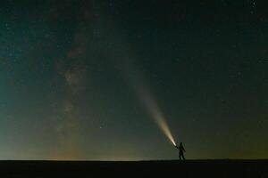 retour vue de homme avec tête lampe de poche permanent sur vert herbeux champ en dessous de magnifique foncé bleu été étoilé ciel. nuit la photographie, beauté de la nature concept. large panorama, copie espace Contexte. photo