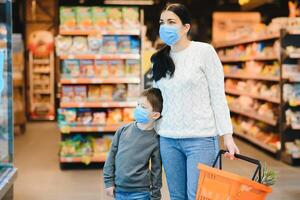 achats avec des gamins pendant virus épidémie. mère et enfant portant chirurgical visage masque achat fruit dans supermarché. maman et peu garçon acheter Frais légume dans épicerie magasin. famille dans magasin photo