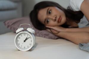 asiatique femme dans lit en retard en essayant à sommeil Souffrance insomnie, sans sommeil ou effrayé dans une cauchemar, à la recherche triste inquiet et stressé. fatigué et mal de crâne ou migraine veille en haut dans le milieu de le nuit. photo