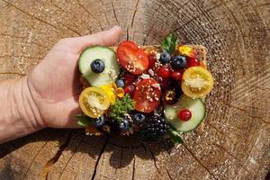 tranche de pain de blé entier sain sans sucre avec de petits concombres, tomates et baies sur la main de la femme. photo