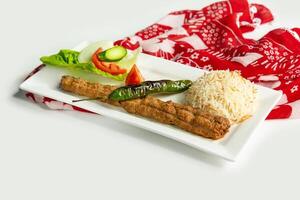 turc style Adana kebab avec riz et salade dans une plat isolé sur coloré table tissu côté vue sur gris Contexte photo