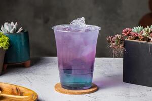 magnifique rêver thé ou glacé violet thé papillon cocktail servi dans jetable verre avec la glace cube isolé sur en bois planche côté vue de taiwanais la glace boisson photo