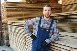 portrait de une Beau ouvrier choisir le meilleur en bois planches. Charpentier permanent suivant à une gros empiler de bois bars dans une entrepôt. photo