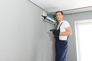 Beau Jeune homme électricien installation air conditionnement dans une client maison photo