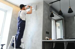 Beau Jeune homme électricien installation air conditionnement dans une client maison photo