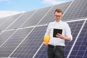 Masculin ingénieur dans casque avec tablette dans mains permanent près solaire panneaux. concept écologie protection. photo