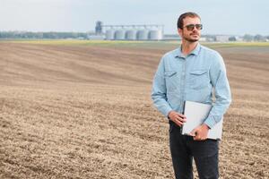 content agriculteur avec portable permanent dans blé champ dans de face de grain silo photo