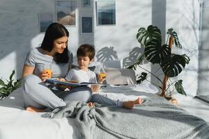 magnifique femme avec sa fils en buvant jus dans le Matin dans lit. en bonne santé en mangeant concept photo