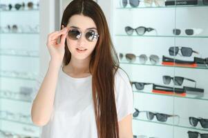 une Jeune femme choisit sur des lunettes de soleil dans un optique boutique photo