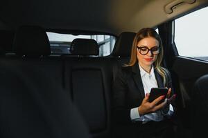 certains Trier de intéressant information. intelligent femme d'affaires est assis à banquette arrière de le luxe voiture avec noir intérieur. photo