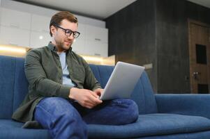 côté vue Beau Jeune homme d'affaire dans lunettes travail avec ordinateur. agréable content homme communicant dans social réseau, recherche information en ligne photo