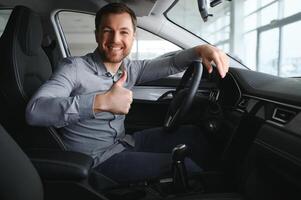 réussi et heureux. coup de une content mature homme souriant à le caméra séance dans le sien marque Nouveau voiture à le local concession photo