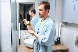 Beau Jeune homme appliquant crème sur le sien visage dans salle de bains photo