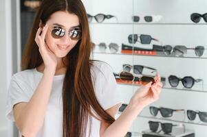 une Jeune femme choisit sur des lunettes de soleil dans un optique boutique photo