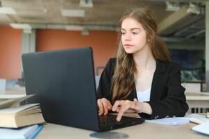 une magnifique caucasien femelle étudiant est en train d'étudier dans Université à distance. elle est séance avec une portable et une bloc-notes et concentré est en train de regarder une vidéo conférence leçon photo