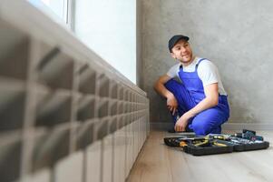 Jeune homme plombier vérification radiateur tandis que installation chauffage système dans appartement photo