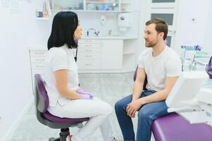 Beau homme souriant tandis que les dents examen. content Masculin patient séance dans une dentiste chaise et ayant vérifier en haut dents. photo