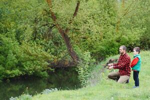 une père enseignement le sien fils Comment à poisson sur une rivière à l'extérieur dans été ensoleillement photo