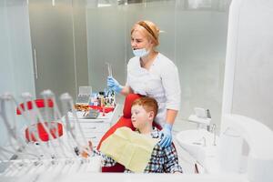 pédiatrique dentiste examiner une peu garçons les dents dans le dentistes chaise à le dentaire clinique photo