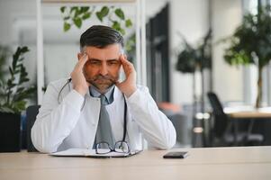 mature médecin homme à le clinique fatigué frottement nez et yeux sentiment fatigue et mal de tête. stress et frustration concept. photo