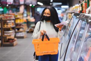 africain femme portant jetable médical masque. achats dans supermarché pendant coronavirus pandémie épidémie. épidémie temps photo