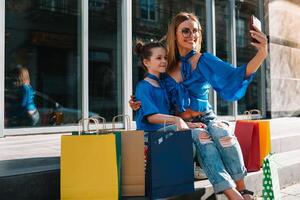 magnifique maman et sa mignonne peu fille sont en portant achats Sacs, à la recherche à caméra et souriant tandis que permanent en plein air. achats concept. photo