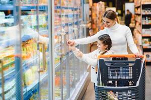 famille dans le supermarché. magnifique Jeune maman et sa peu fille souriant et achat aliments. le concept de en bonne santé alimentaire. récolte photo