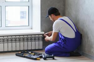 Jeune homme plombier vérification radiateur tandis que installation chauffage système dans appartement photo