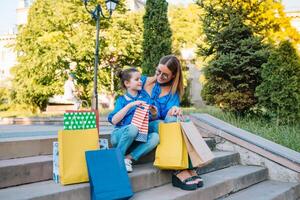 magnifique maman et sa mignonne peu fille sont en portant achats Sacs, à la recherche à caméra et souriant tandis que permanent en plein air. achats concept photo