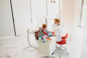 pédiatrique dentiste examiner une peu garçons les dents dans le dentistes chaise à le dentaire clinique photo