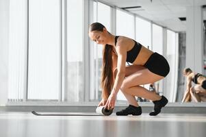 temps pour méditation, aptitude session, bien-être concept. fille portant gris sportif un pantalon roulant aptitude tapis avant, après classe dans yoga studio club ou à Accueil sur en bois sol. photo