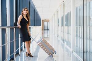 de face vue de une voyageur femme en marchant porter une valise dans un aéroport couloir photo