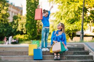 Jeune mère et sa fille Faire achats ensemble. femme avec fille enfant après achats dans rue. femme avec fille avec achats Sacs en plein air. femme et sa fille après achats. photo