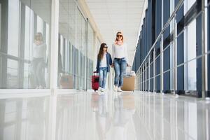 content Jeune mère et sa fille en marchant dans le aéroport Terminal tandis que porter une valise. haute saison et vacances concept. se détendre et modes de vie photo