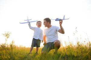 papa avec le sien fils à le coucher du soleil dans la nature. une père pièces avec jouet avions avec le sien fils à le coucher du soleil. du père journée photo