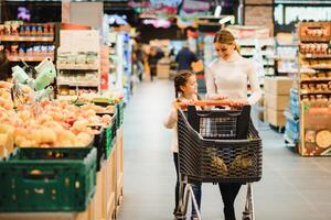 famille dans le supermarché. magnifique Jeune maman et sa peu fille souriant et achat aliments. le concept de en bonne santé alimentaire. récolte photo