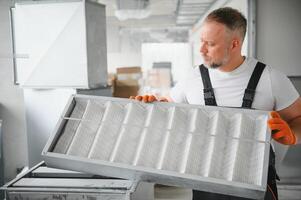 une Masculin ouvrier détient un air filtre pour air conditionnement dans un Bureau espace. installation de un air Conditionneur. photo