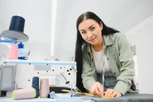 Jeune couturière femme coud vêtements sur travail tableau. souriant couturière et sa main proche en haut dans atelier. photo