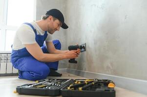 sur de soi professionnel électricien dans uniforme en utilisant Tournevis tandis que remplacer une prise dans appartement après rénovation travail photo