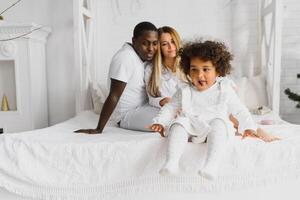 excité multiracial Jeune famille avec peu fille enfant avoir amusant, fou de joie heureux. international maman et papa jouer avec petit fille, prendre plaisir fin de semaine à Accueil ensemble photo