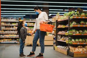 mère et sa fils portant protecteur visage masque magasin à une supermarché pendant le coronavirus épidémie. photo