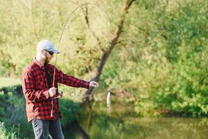 pêcheur par le rivière avec une capture de poisson. homme pêcheur détient dans main poisson. photo